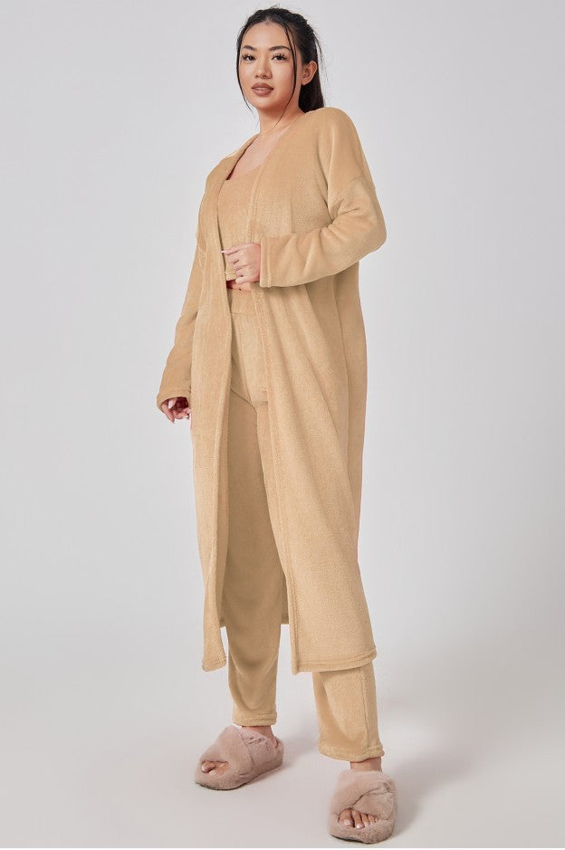 Woman wearing a beige loungewear set with pink slippers on a white background